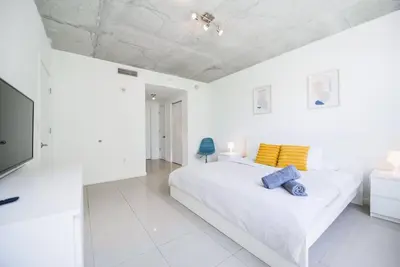 a white bedroom with a large bed with yellow and blue pillows at Awesome Apt With Pool in Midtown Miami in Miami