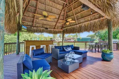 a patio with blue chairs and a straw roof at Spacious home wprivate pool game room in Plantation