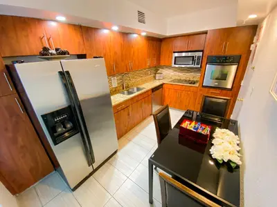 a kitchen with a stainless steel refrigerator and a table at Hollywood Beachfront Condo, Steps to Ocean, Pool & Game Room in Hollywood
