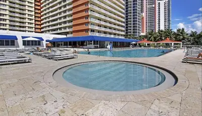 a large swimming pool with chairs and buildings at Ramada Marco Polo Beach in Miami Beach