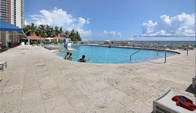 a swimming pool with people in it next to the ocean at Ramada Marco Polo Beach in Miami Beach