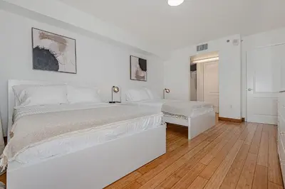 a white bedroom with two beds and a wooden floor at Lovely condo with city & ocean views. Sleep up to 6 people! in Miami