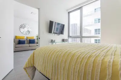 a white bedroom with a yellow bed and a tv at Amazing Condo in Downtown Miami/Brickell w/PARKING in Miami