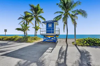 a blue life guard shack on a beach with palm trees at Waves On Desoto Rental Unit With Pool in Hollywood