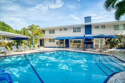 a swimming pool in front of a building with chairs and umbrellas at Casa Cordova Apartments By Lowkl in Fort Lauderdale