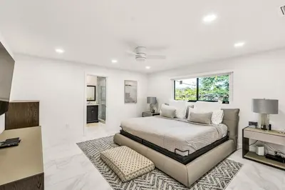 a white bedroom with a bed and a rug at Sandals Beach Cottage in Fort Lauderdale