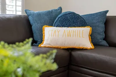 a pillow that says stay awhile on a couch at Victoria Park Oasis with Heated Pool and More in Fort Lauderdale