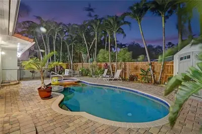a swimming pool in a backyard with palm trees at Chic Victoria Park Villa with Heated Pool and Spa in Fort Lauderdale