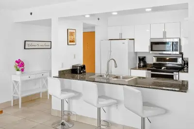 a kitchen with white cabinets and a counter with stools at 2 Bedroom, 2 Bathroom plus Den Brickell Condo Pool, Hot Tub, and Gym in Miami