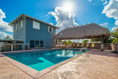 a swimming pool in front of a house with a thatch roof at Beautiful 7-Bedroom Villa with Pool in Hialeah