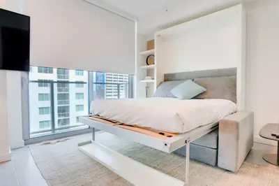 a white bedroom with a large bed and a large window at Modern and newly built studio with Pool, Gym, and Restaurant access in Miami