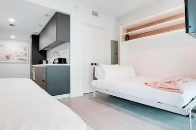 a white bedroom with two beds and a kitchen at Modern and newly built studio with Pool, Gym, and Restaurant access in Miami