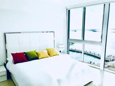 a white bed with colorful pillows in a room with a window at Amazing unit Miami Brickell with Sea & City View in Miami