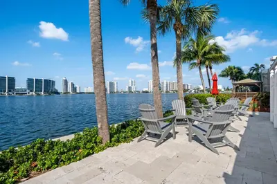 a row of chairs and palm trees next to a body of water at Waterfront Luxury 2-Bedroom Condo Sunny Isles Beach in Miami Beach