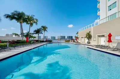 a swimming pool at a hotel with chairs and palm trees at Waterfront Luxury 2-Bedroom Condo Sunny Isles Beach in Miami Beach