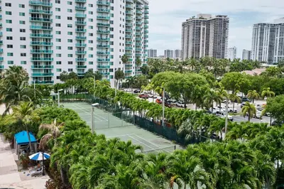 a tennis court with palm trees and buildings at MIAMI Collins Beach Apartments in Sunny Isles Beach