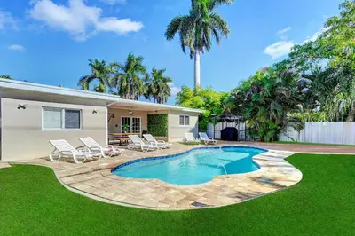 a backyard with a swimming pool and chairs and a house at Great Location 5BR Heated Pool near Hollywood Beach in Hollywood