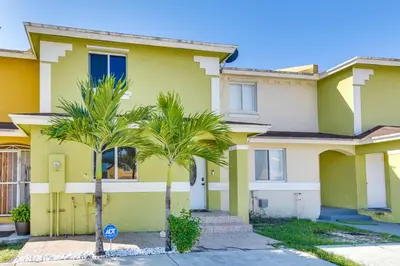 a yellow house with two palm trees in front of it at Opa-locka Townhome, 15 Mi to Miami Beach! in Opa-locka
