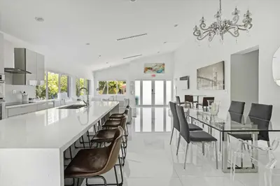 a white kitchen with a long counter and chairs at Luxury House 4 beds heated Pool w Jaccuzzi in North Bay Village