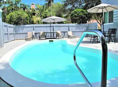a blue swimming pool with chairs and umbrellas at Walk to Las Olas Pool Perfect Couples Stay in Fort Lauderdale