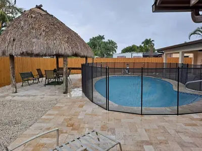 a swimming pool with a straw umbrella and a table at Pool home in Miami in Tamiami