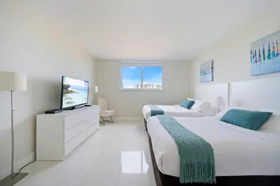 a white bedroom with two beds and a tv at Ocean Reserve 1524 in Miami Beach