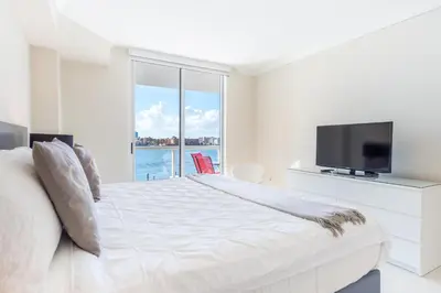 a white bedroom with a large bed and a tv at Golden Bay 406 in Miami Beach