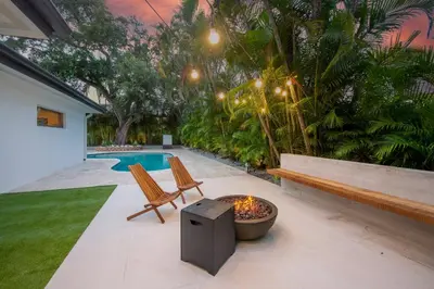 a patio with a fire pit and two chairs and a pool at Super Fun Villa Game Room BY THE GLAMHOMES in North Miami Beach