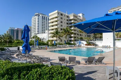 a swimming pool with chairs and a blue umbrella at Decoplage Paradise - Main Home in Miami Beach