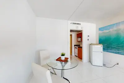 a white kitchen with a glass table and a refrigerator at Decoplage Paradise - Unit A in Miami Beach
