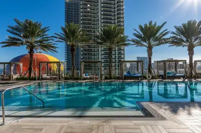 a swimming pool with palm trees and a tall building at The Ultimate Resort - BEACHFRONT 2 BEDROOM APARTMENT WITH DIRECT OCEAN VIEW, ROOFTOP POOL, HOT TUB AND GYM in Hollywood