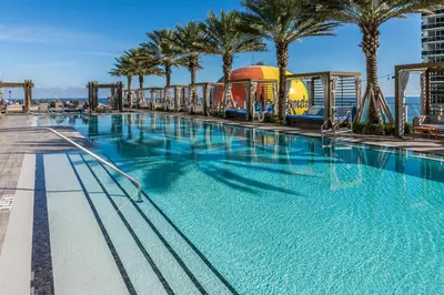 a large swimming pool with palm trees and a roller coaster at Picturesque Beachfront Condo - LOVELY 2BD and 2BA APT WITH DIRECT OCEAN VIEW in Hollywood