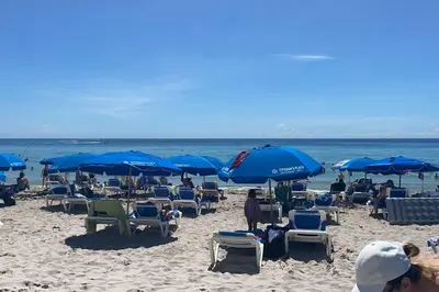 a group of people sitting on a beach with blue umbrellas at BeachWalk Studio Apt with Beach Service 03B in Hallandale Beach