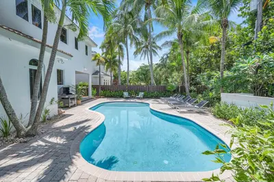 a swimming pool in front of a house with palm trees at Steps from the Beach Heated Pool Sun Key Game room RESlDENCES in Fort Lauderdale