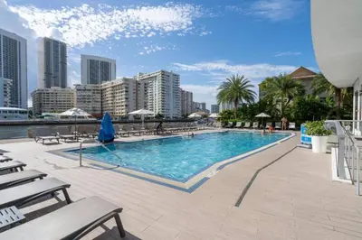 a large swimming pool with chairs and a city at Modern Beach Studio, 2 Full Beds, Prime Location in Hallandale Beach